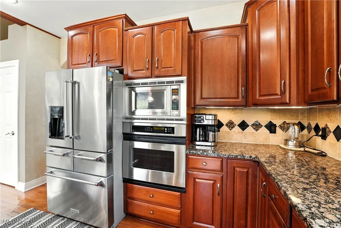 Kitchen featuring stainless steel appliances, dark stone counters, light wood finished floors, tasteful backsplash, and ornamental molding