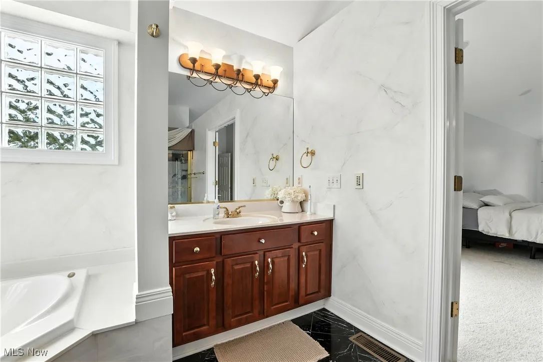 Ensuite bathroom featuring vanity, a bath, and marble finish flooring