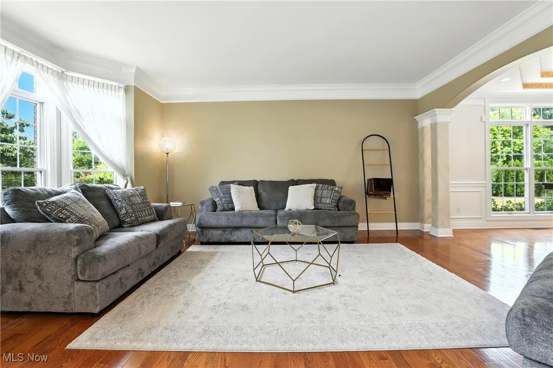 Living area with ornamental molding, arched walkways, decorative columns, and wood finished floors