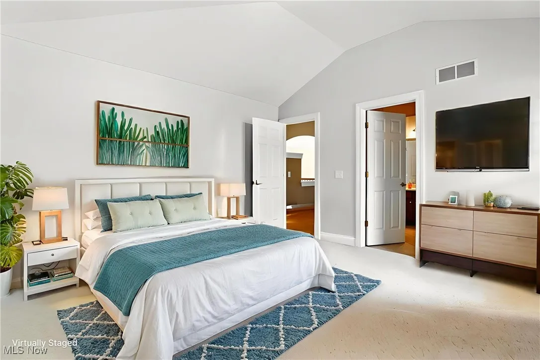 Bedroom with vaulted ceiling, arched walkways, and light colored carpet