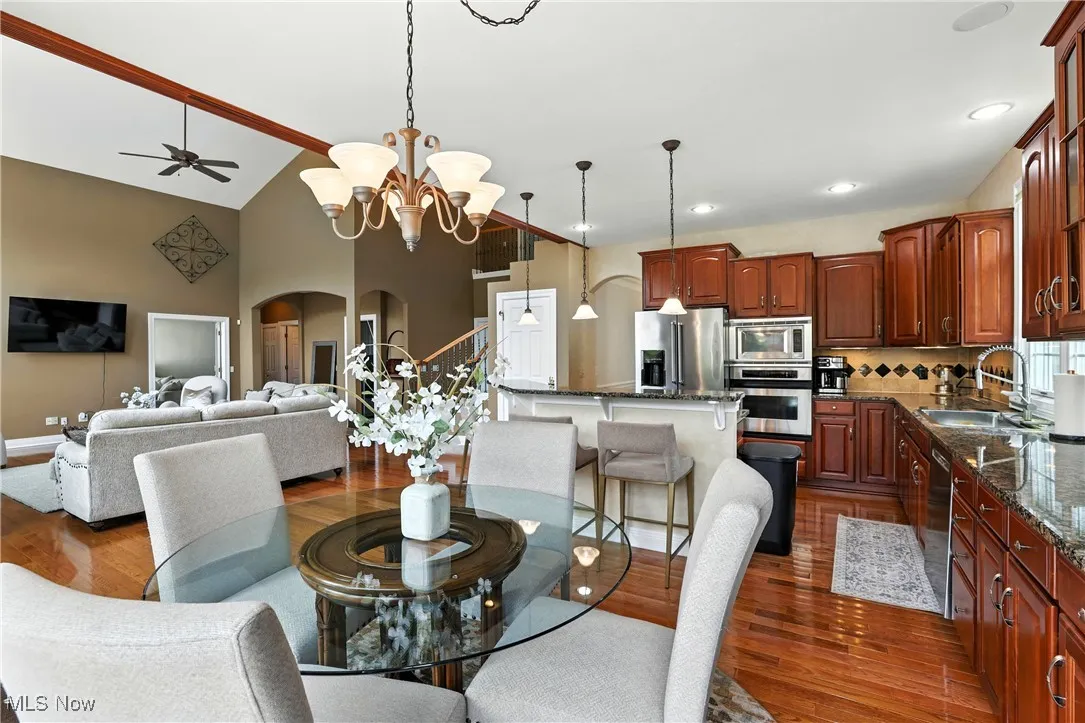 Dining area featuring arched walkways, dark wood-style flooring, a ceiling fan, a chandelier, and high vaulted ceiling