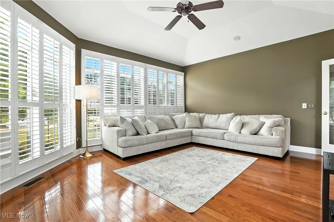 Living area with ceiling fan, wood finished floors, a tray ceiling, and vaulted ceiling