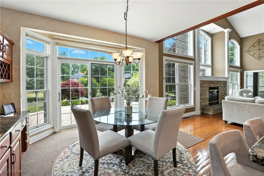 Dining space with plenty of natural light, a chandelier, a stone fireplace, light wood-style flooring, and lofted ceiling