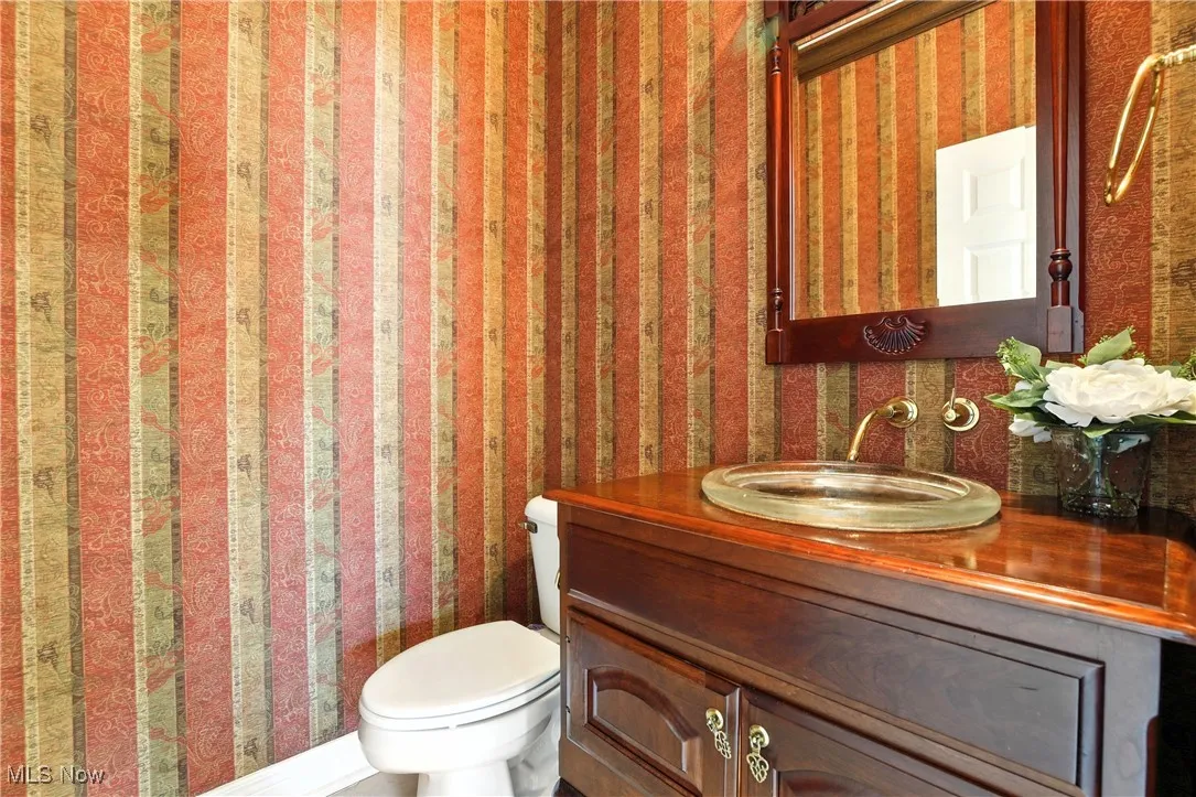 Half bath featuring wallpapered walls and vanity