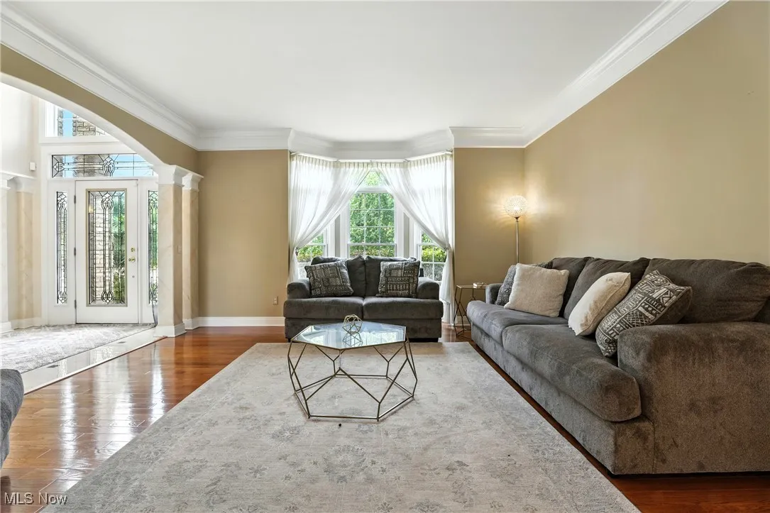 Living room with arched walkways, decorative columns, ornamental molding, and wood finished floors