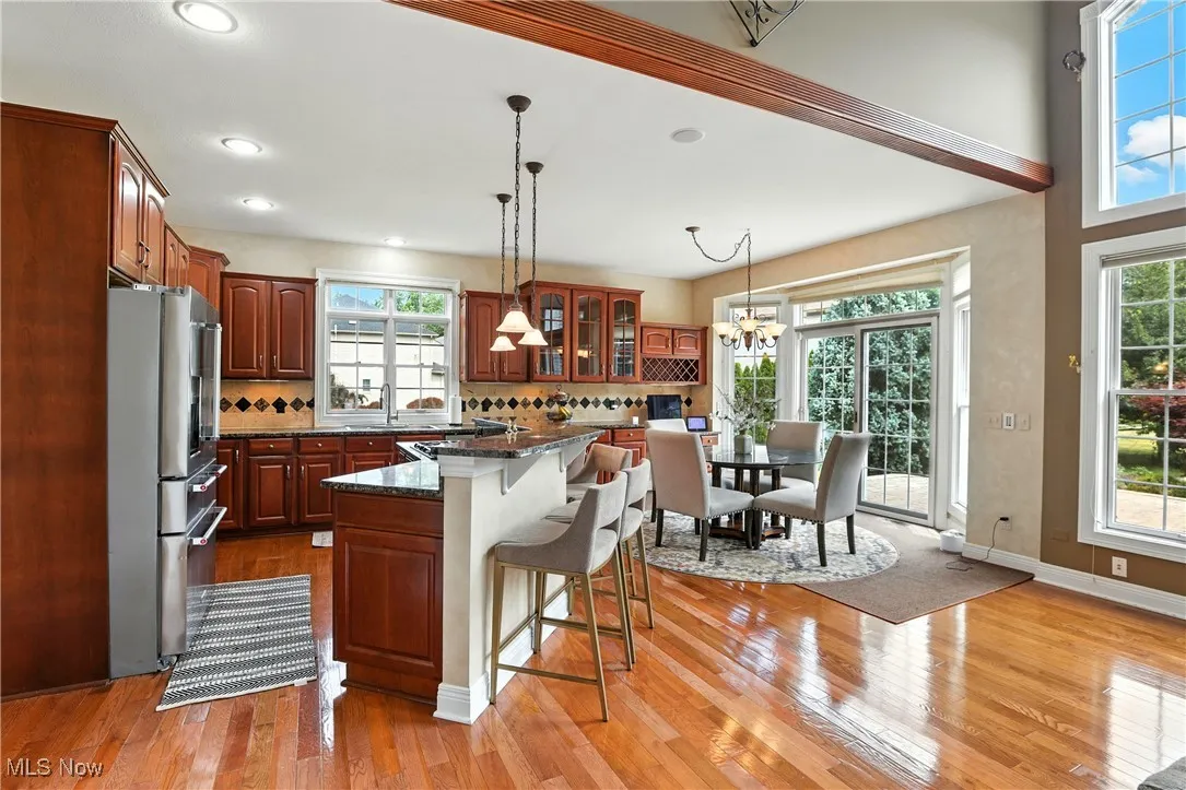 Kitchen with freestanding refrigerator, a kitchen breakfast bar, light wood-type flooring, glass insert cabinets, and backsplash