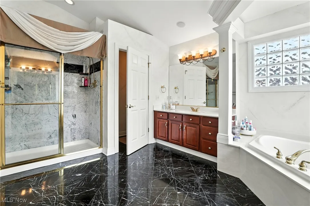 Full bathroom with marble tiled floors, a bath, vanity, a marble finish shower, and ornate columns