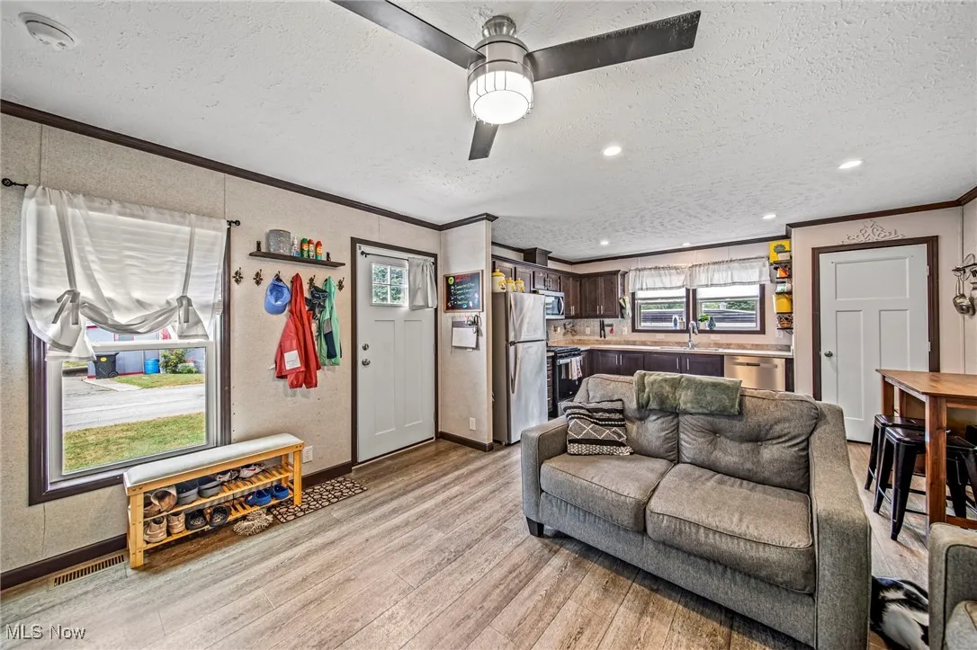 Living room with ornamental molding, light wood-type flooring, a textured ceiling, a ceiling fan, and recessed lighting