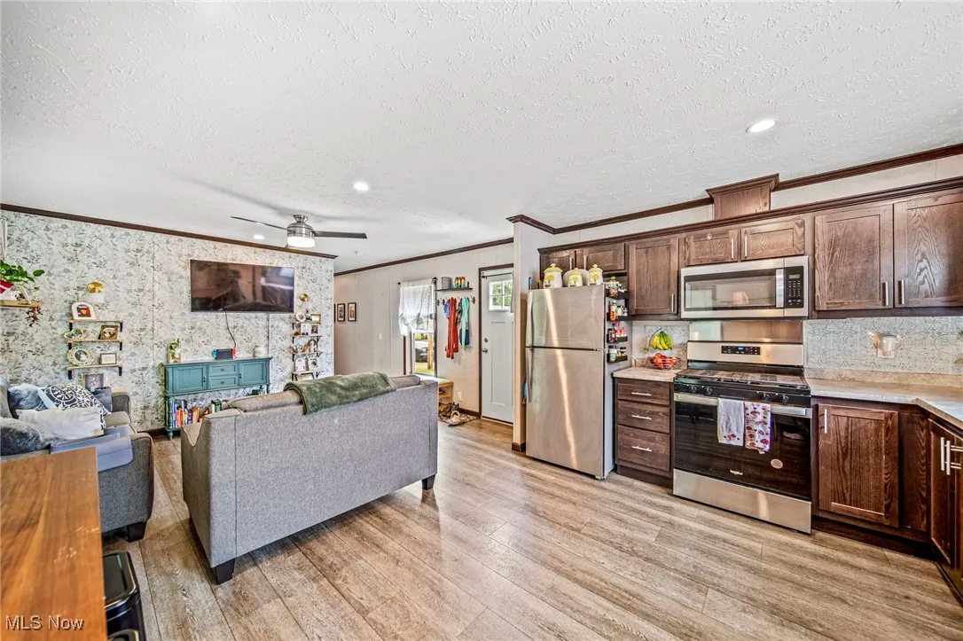 Kitchen featuring ornamental molding, appliances with stainless steel finishes, open floor plan, light wood-style flooring, and light countertops