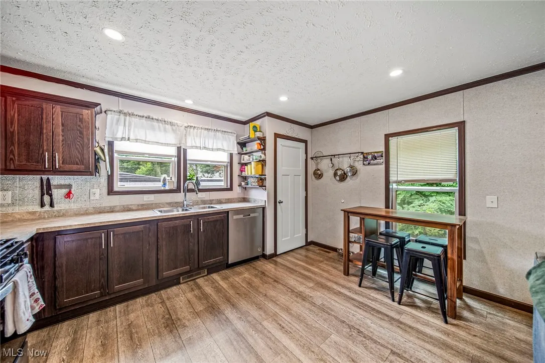 Kitchen with ornamental molding, light wood finished floors, appliances with stainless steel finishes, light countertops, and dark brown cabinets