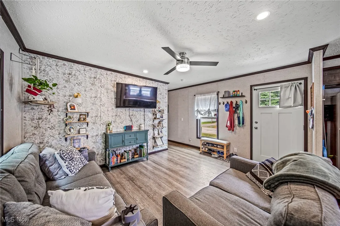 Living room featuring ornamental molding, wood finished floors, a textured ceiling, and a ceiling fan