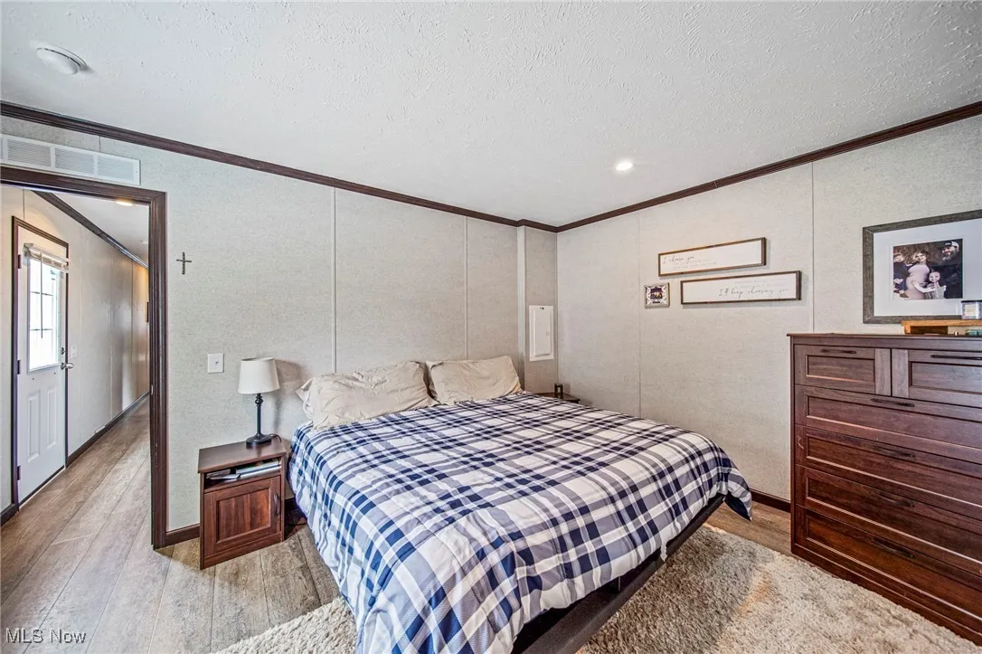 Bedroom with ornamental molding, light wood-type flooring, and a textured ceiling