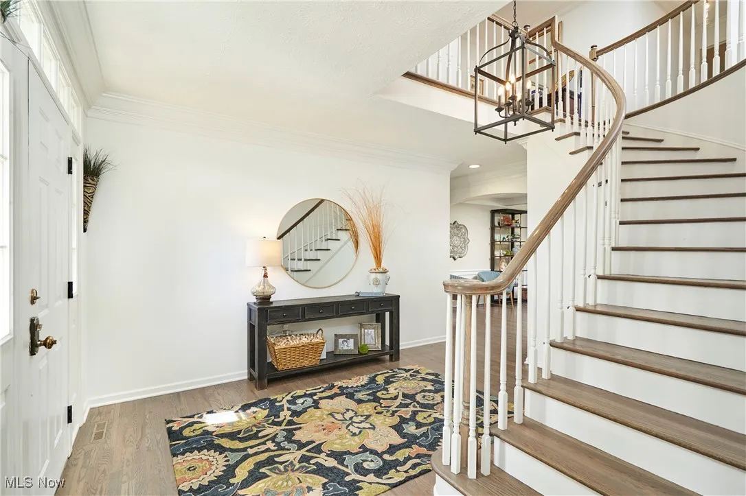 Foyer with stairs, a chandelier, wood finished floors, crown molding, and recessed lighting