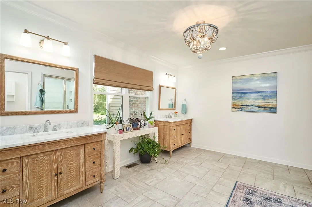 Full bath with two vanities, ornamental molding, and a chandelier