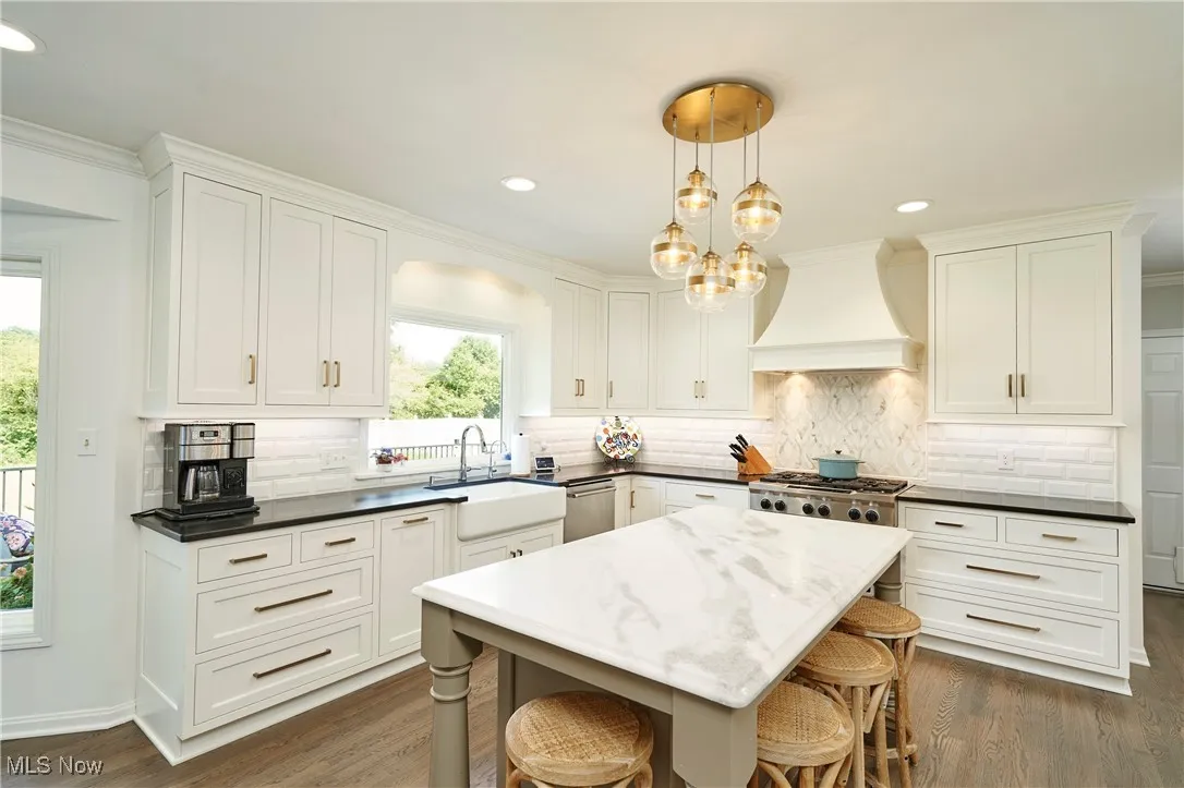 Kitchen featuring dark wood finished floors, premium range hood, a kitchen bar, white cabinets, and recessed lighting