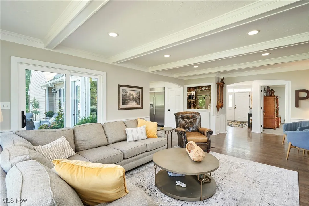 Living room featuring arched walkways, beam ceiling, wood finished floors, crown molding, and recessed lighting