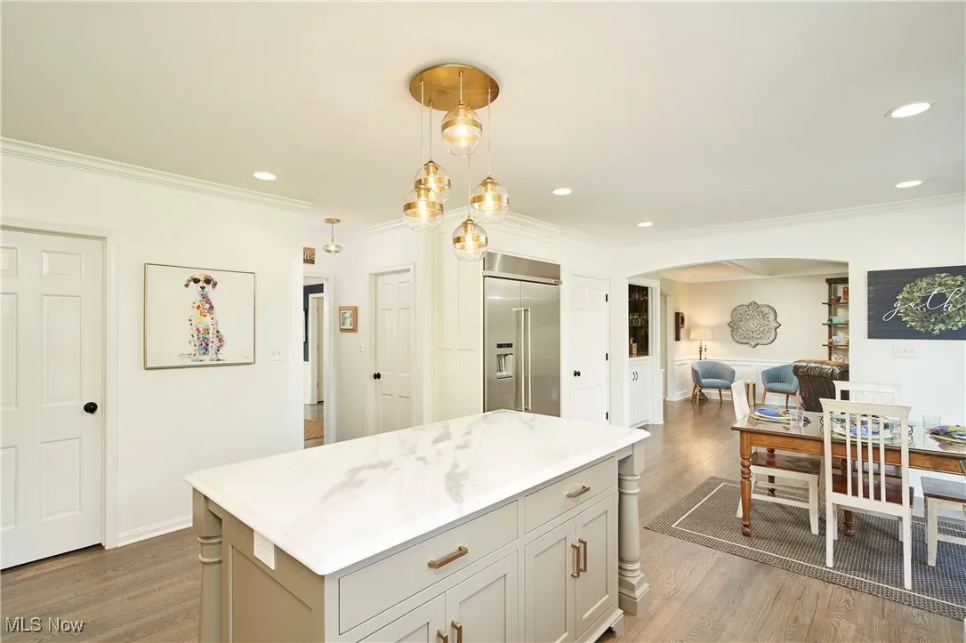 Kitchen featuring arched walkways, ornamental molding, wood finished floors, built in fridge, and a center island