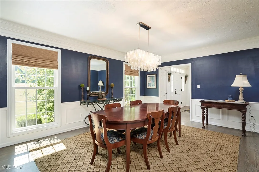 Dining room with wainscoting, a chandelier, wood finished floors, a decorative wall, and ornamental molding