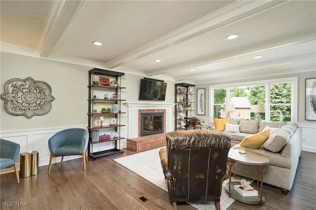 Living area with beam ceiling, ornamental molding, a brick fireplace, a decorative wall, and wood finished floors