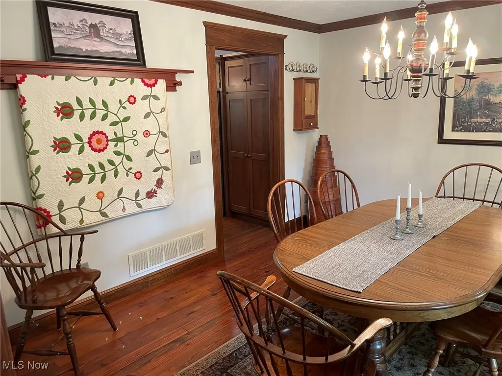 Dining area with a chandelier, dark wood-type flooring, and ornamental molding