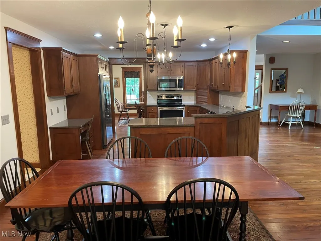 Kitchen with dark wood-style flooring, stainless steel appliances, a chandelier, dark countertops, and decorative light fixtures