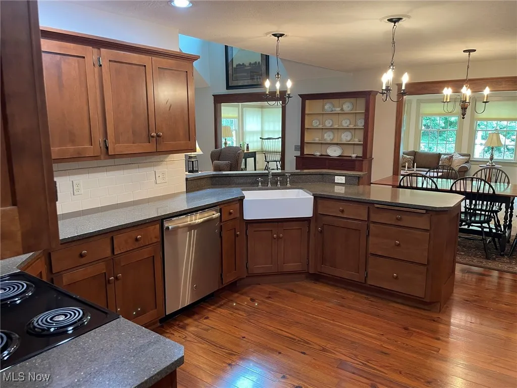 Kitchen featuring a chandelier, a peninsula, dishwasher, and dark wood-type flooring