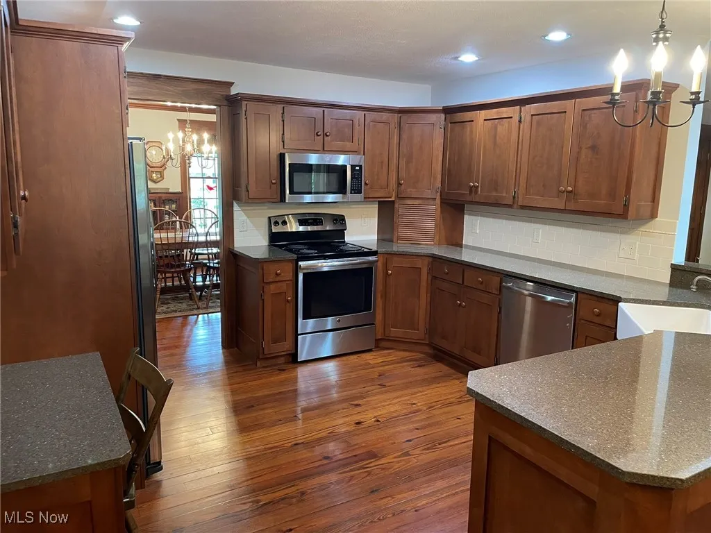 Kitchen featuring a chandelier, stainless steel appliances, dark wood-type flooring, hanging light fixtures, and backsplash