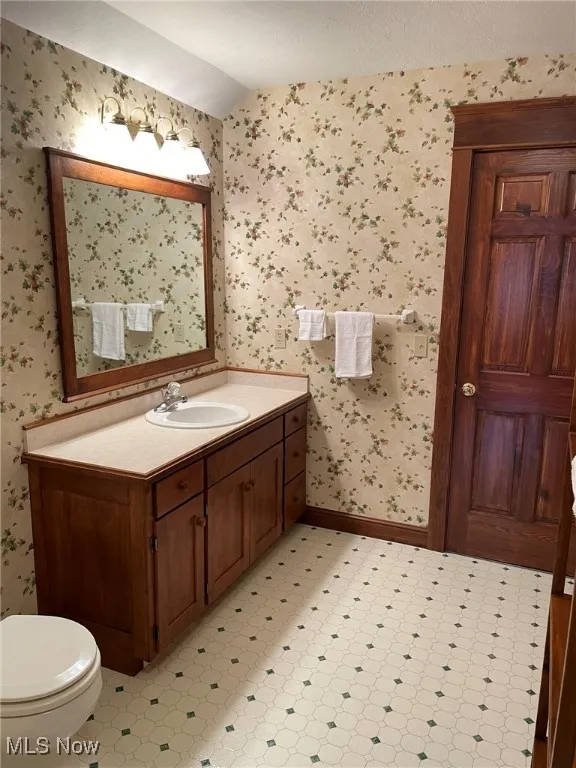Half bath with wallpapered walls, vanity, lofted ceiling, and tile patterned floors