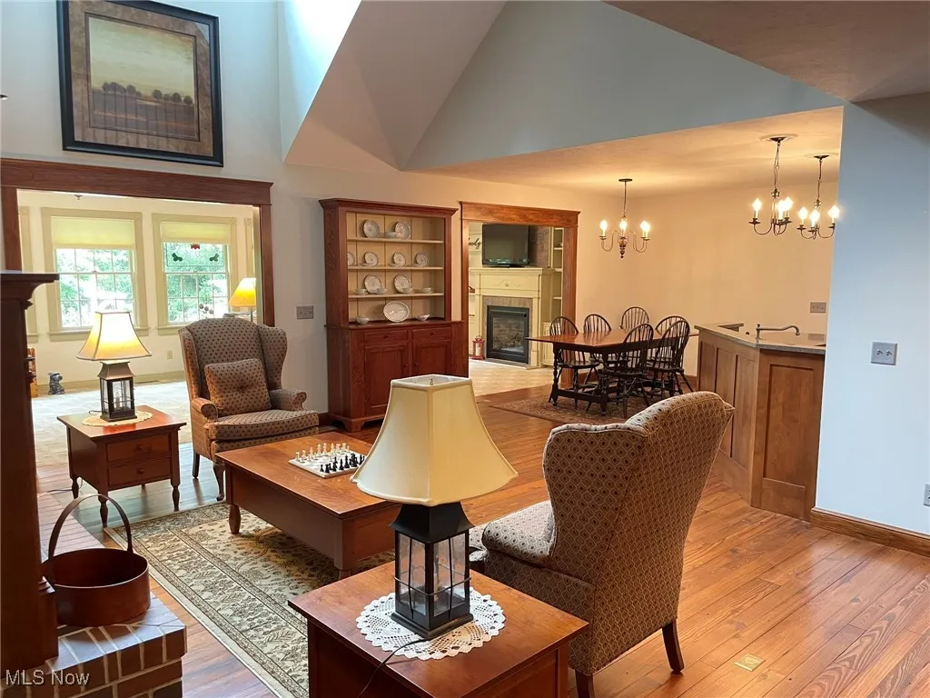 Living room with a fireplace, light wood-type flooring, a chandelier, and vaulted ceiling