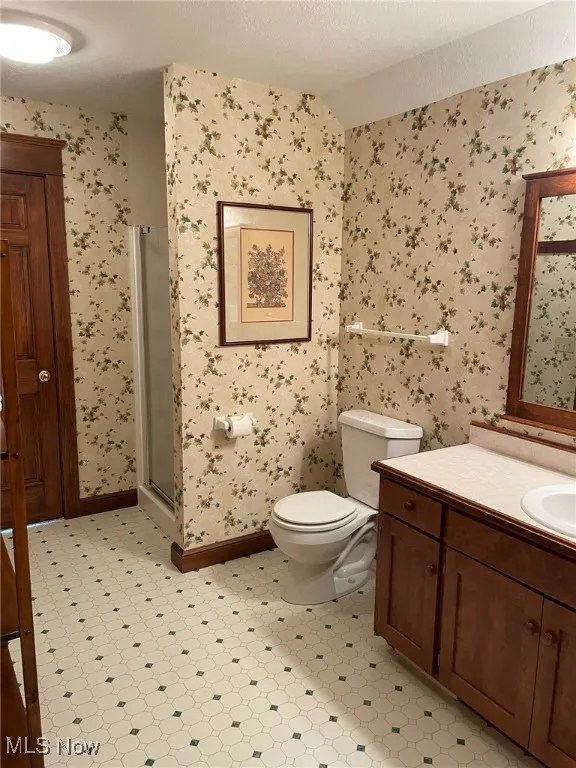 Bathroom with wallpapered walls, vanity, a stall shower, vaulted ceiling, and tile patterned floors