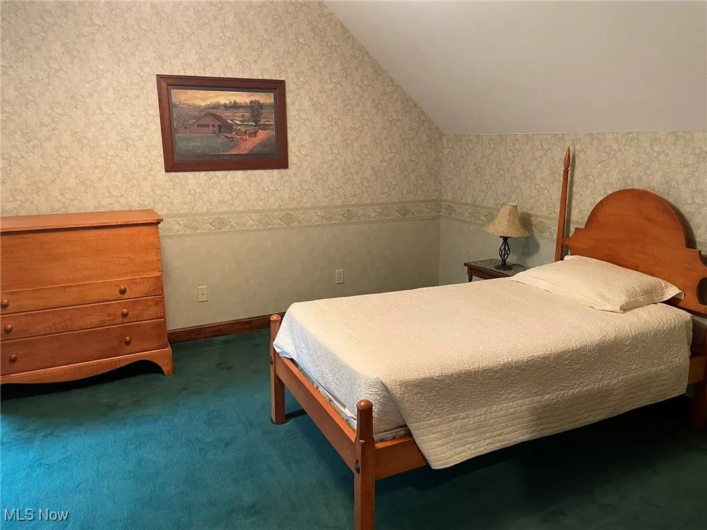 Bedroom with vaulted ceiling, carpet flooring, and wallpapered walls