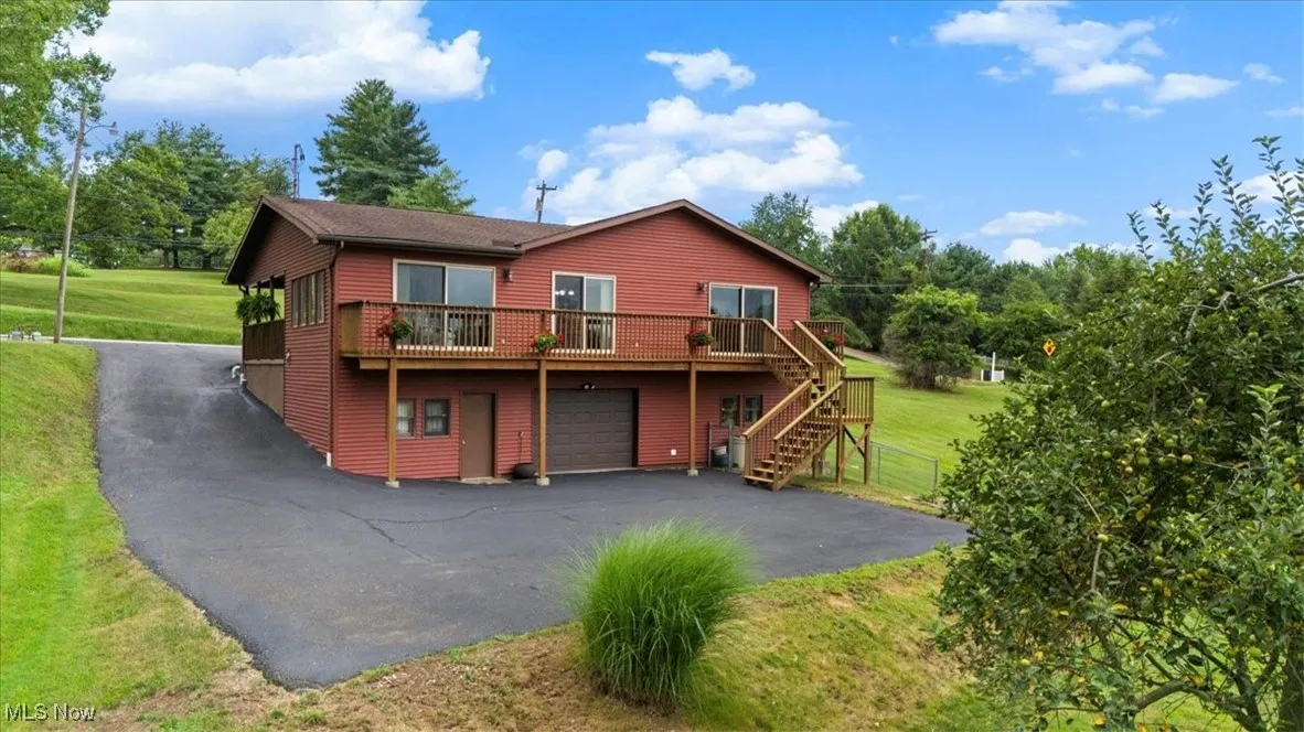 Back of house with driveway, stairway, an attached garage, a lawn, and a deck. Plenty of room for extra parking.