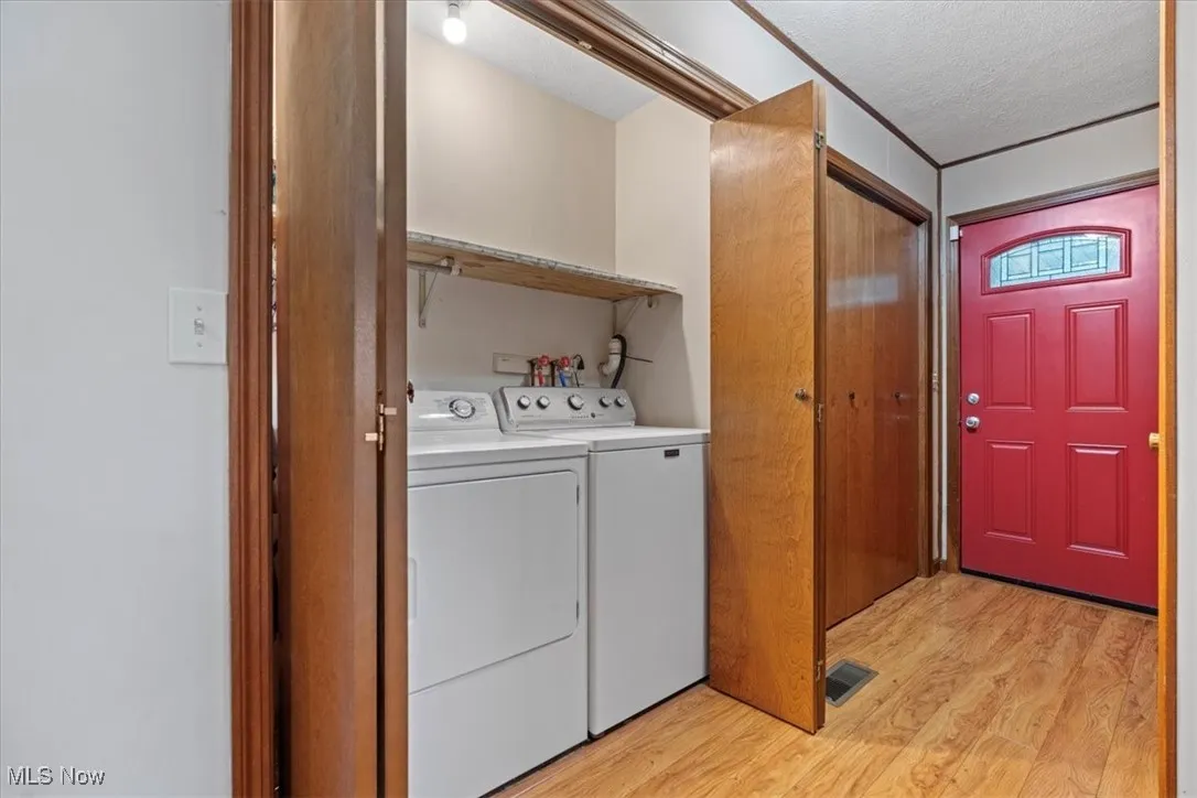  First floor Laundry room with light wood-type flooring, washing machine and clothes dryer, and a textured ceiling.  Washer and Dryer stays with the house.
