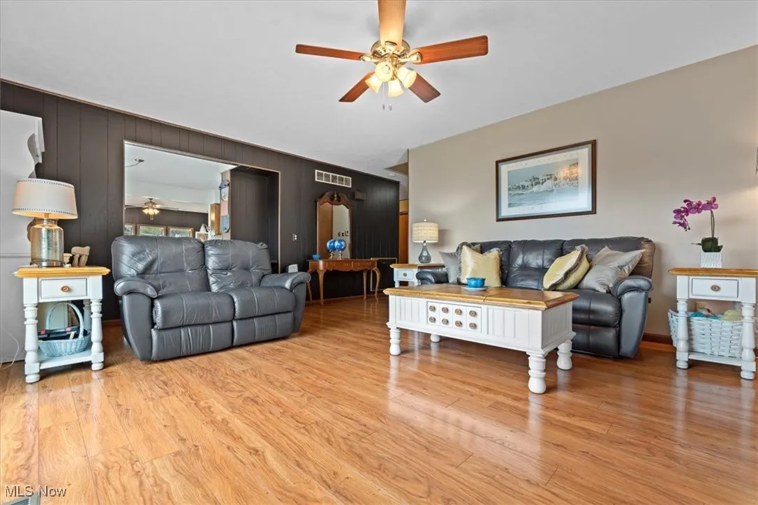Living room featuring ceiling fan, light wood-type flooring, arched walkways, and wood walls.  Open to kitchen and dining room.