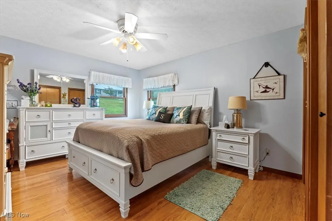 Primary Bedroom with light wood-type flooring, ceiling fan, and a textured ceiling.  On right side of the room is 3 4 closets.
