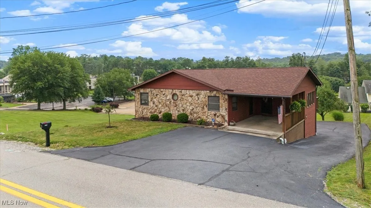 View of front of home with stone siding, driveway, a front yard, and a carport