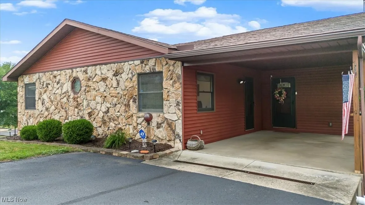 View of front of house featuring stone siding, an attached carport, driveway, and a shingled roof