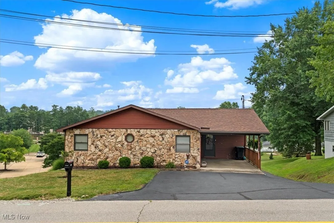 View of front of property featuring asphalt driveway, a front yard, stone siding, and a shingled roof.