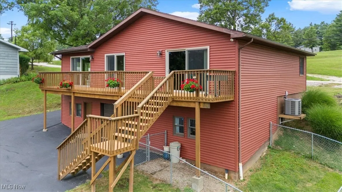 Rear view of property with stairway and a wooden/ TREX decking.  There is a garage and man door to enter the lower level.