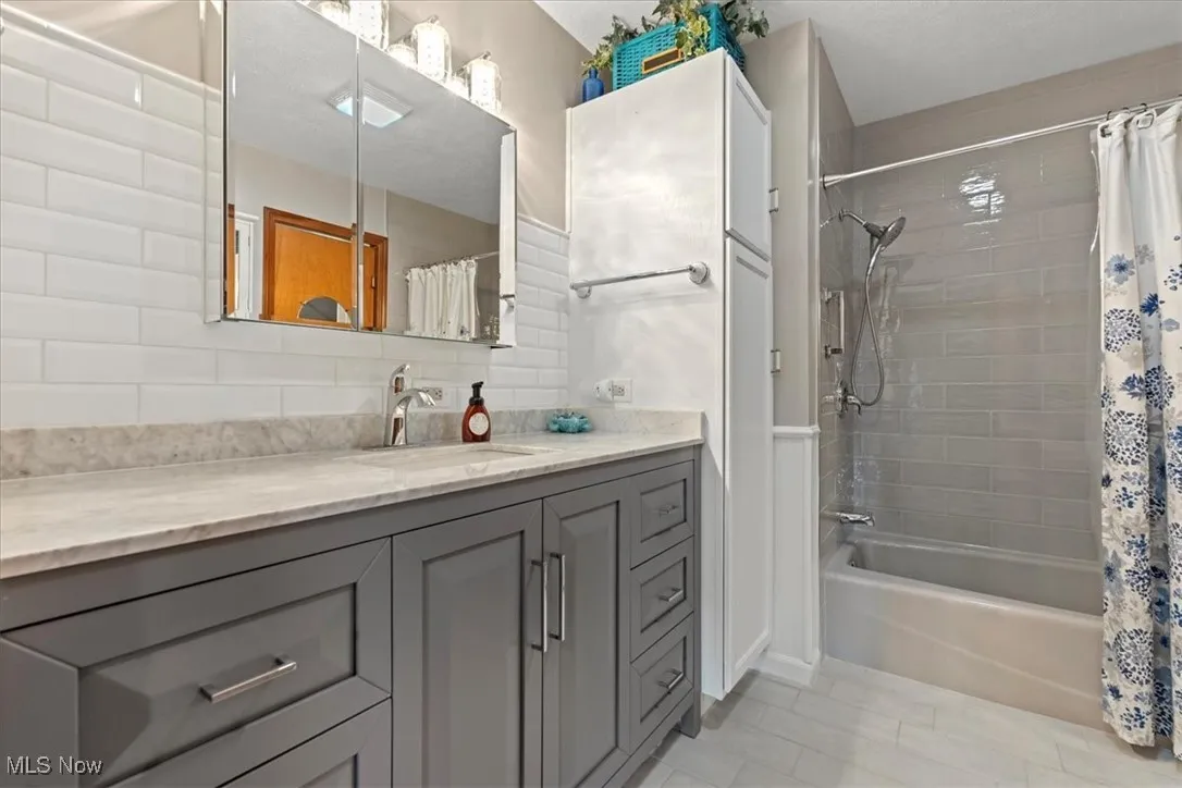Full first floor bathroom with vanity, shower / bathtub combination with curtain, and decorative backsplash