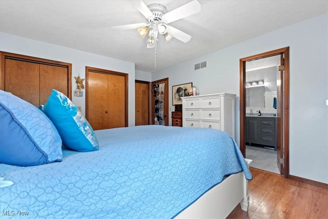 Primary Bedroom featuring light wood-style floors, multiple closets, ensuite bath, and a ceiling fan.