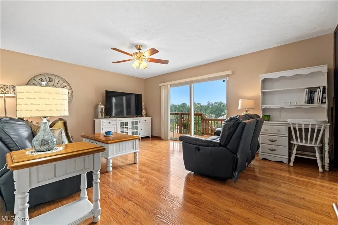 Living area featuring light wood-type flooring, ceiling fan, and a 8 ft. door to the outside deck and stairs to the back driveway and yard.