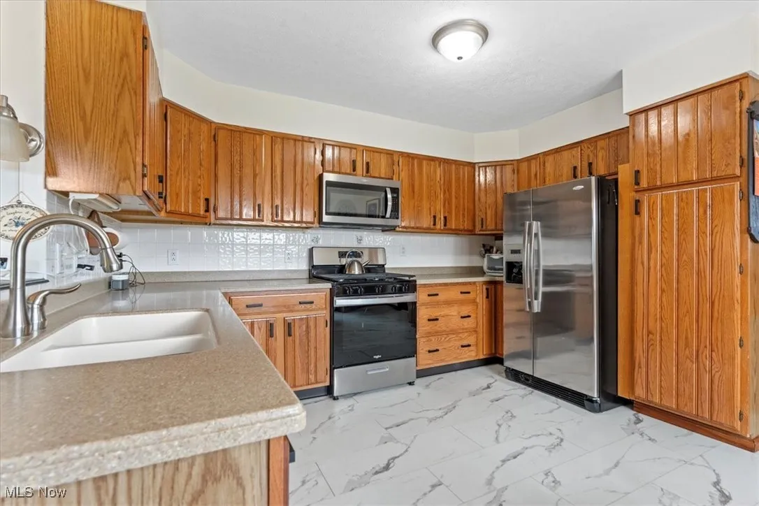 Kitchen with stainless steel appliances, light marble finish floors, and brown cabinets.  The gas range (2025).