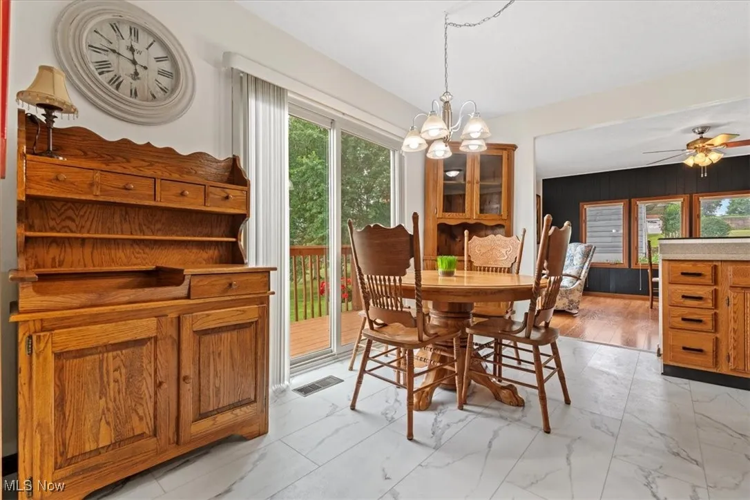Eat in Kitchen featuring light marble finish flooring, a chandelier, ceiling fan, and wood walls.  The Oak corner hutch, table and chairs and sq. hutch stay with the house. This is a 6 ft. sliding door.