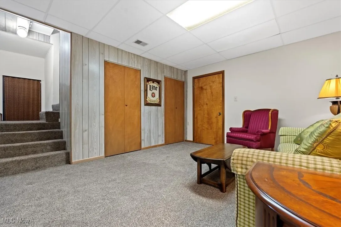 Carpeted den room featuring a drop ceiling, stairway, and wood walls located in the lower walk out level.
