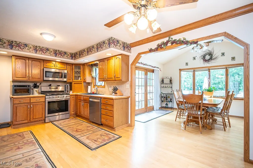 Kitchen with appliances with stainless steel finishes, oak cabinets, light hardwood flooring, ceiling fan, and decorative backsplash