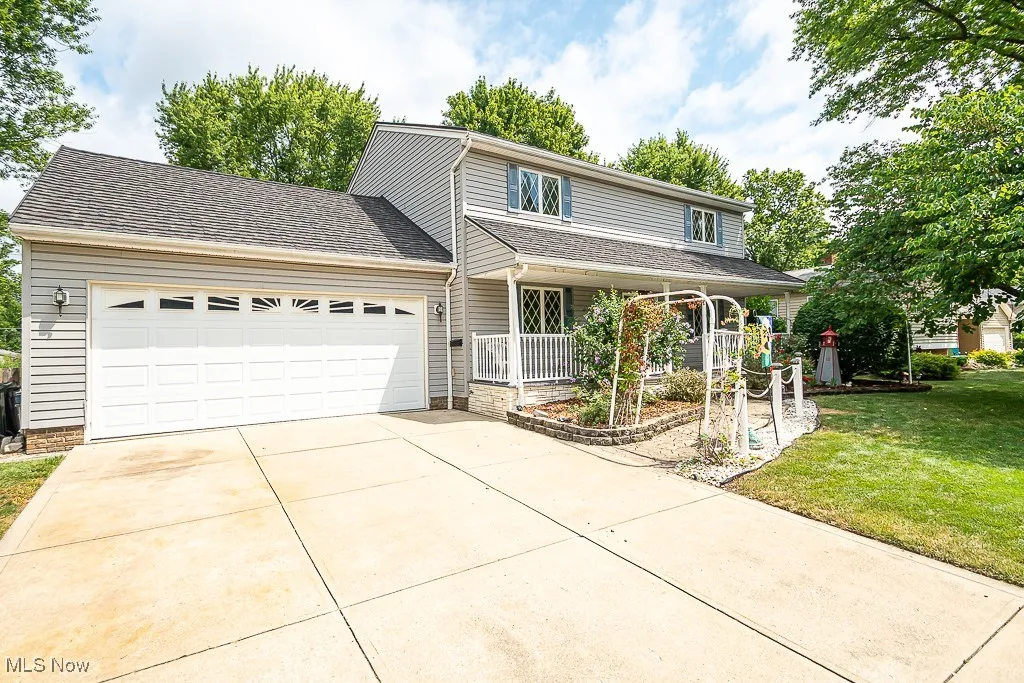 Colonial-style home with an attached garage, concrete driveway, a porch, and front lawn