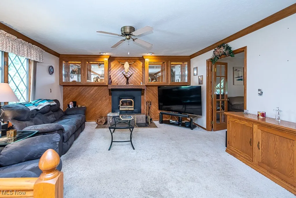 Living area featuring ornamental molding, a ceiling fan, light carpet, and wood walls