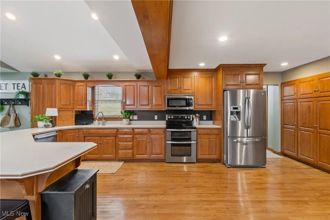 Kitchen with stainless steel appliances, light countertops, a peninsula, brown cabinets, and recessed lighting