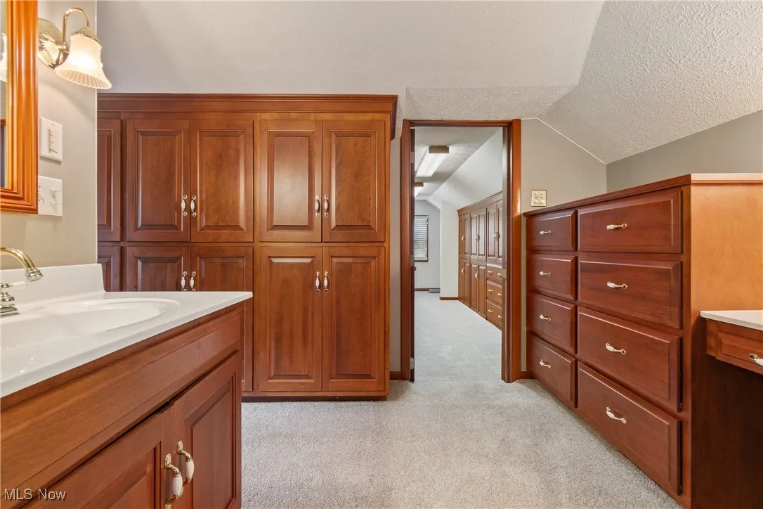 Bathroom with lofted ceiling, a textured ceiling, carpet floors, and vanity